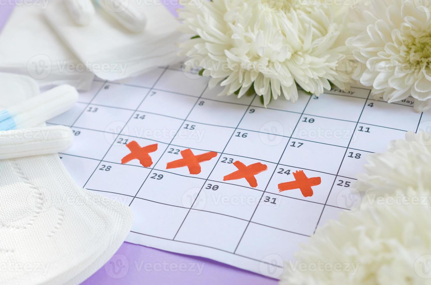 Menstrual pads and tampons on menstruation period calendar with white flowers on lilac background photo