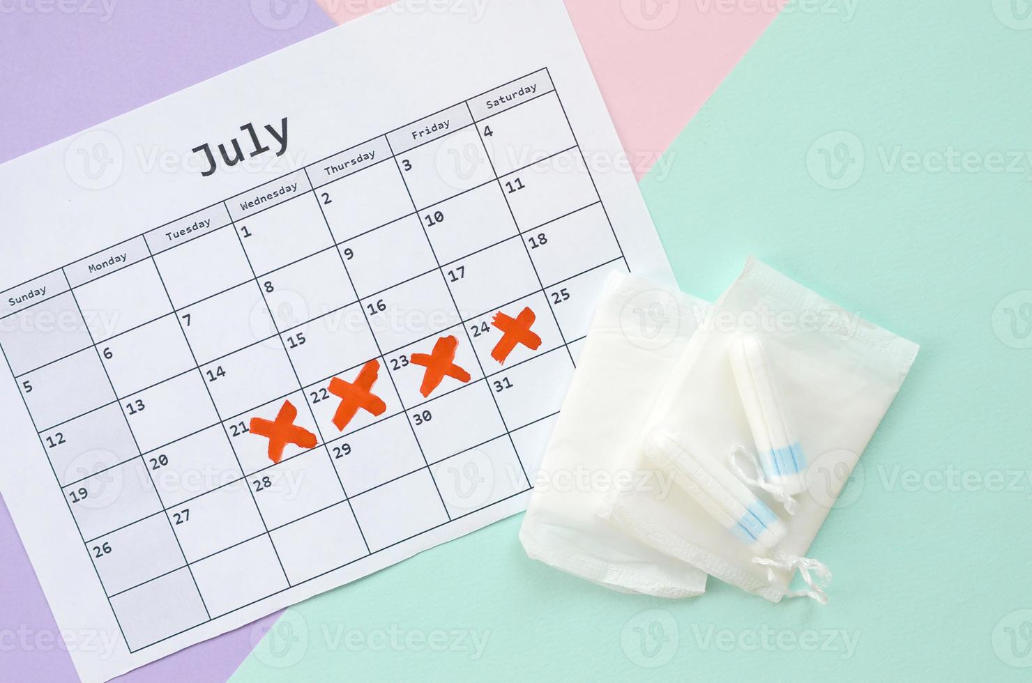 Flat lay composition with calendar and menstrual tampons and pad packs on blue pink and lilac pastel background photo