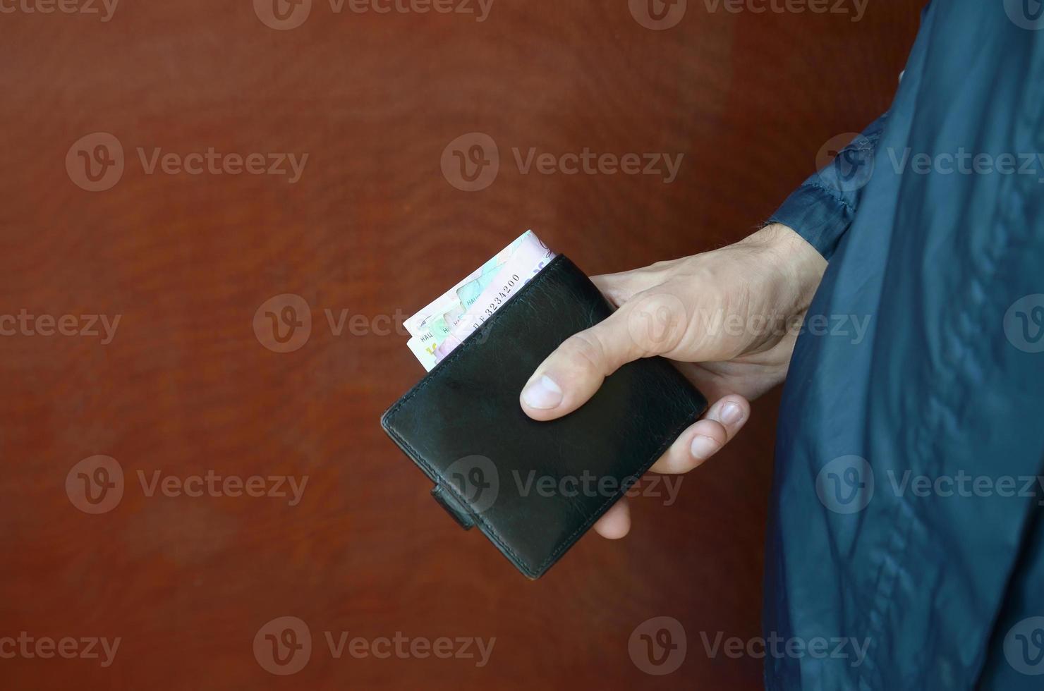 Man holds in hands black leather wallet with ukrainian money or thief who stole wallet full of money photo