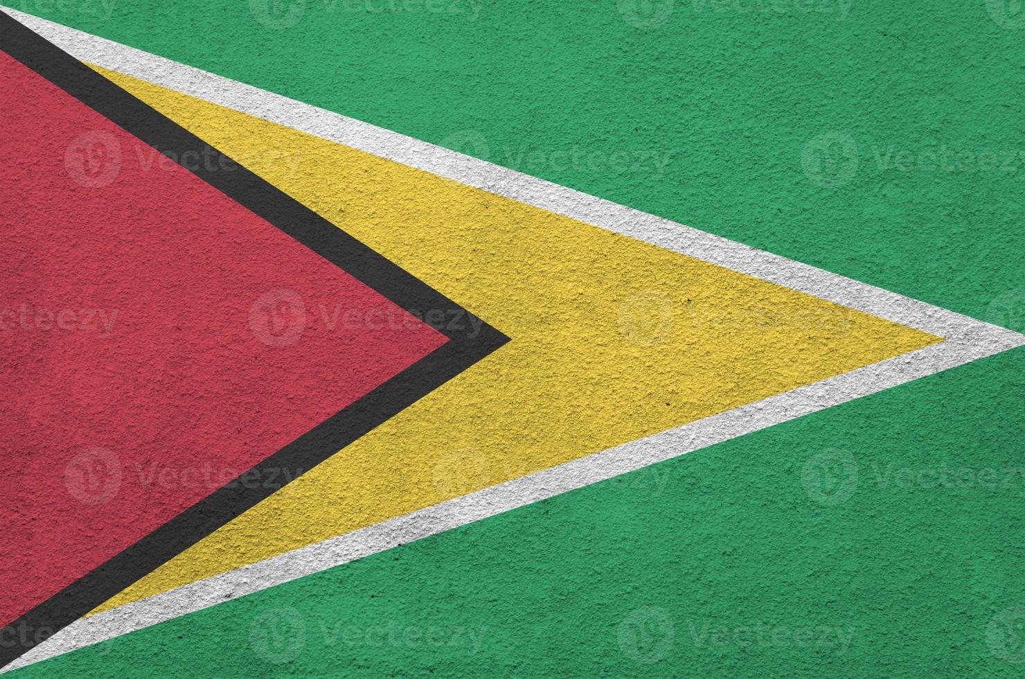 Guyana flag depicted in bright paint colors on old relief plastering wall. Textured banner on rough background photo