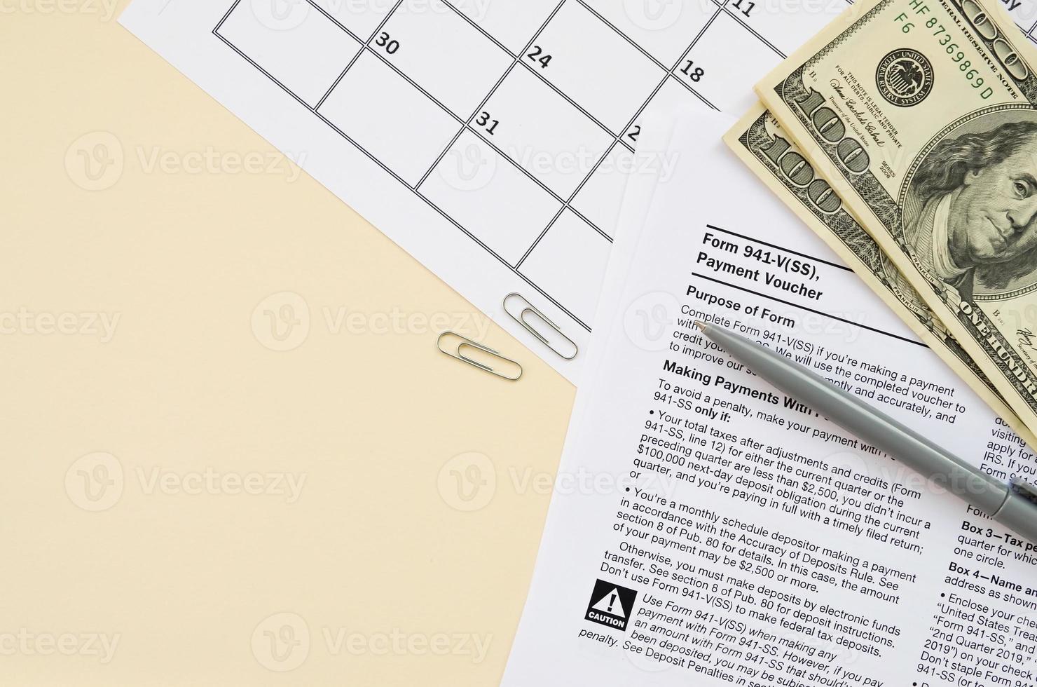 IRS Form 941-V Payment Voucher blank lies with pen and many hundred dollar bills on calendar page photo