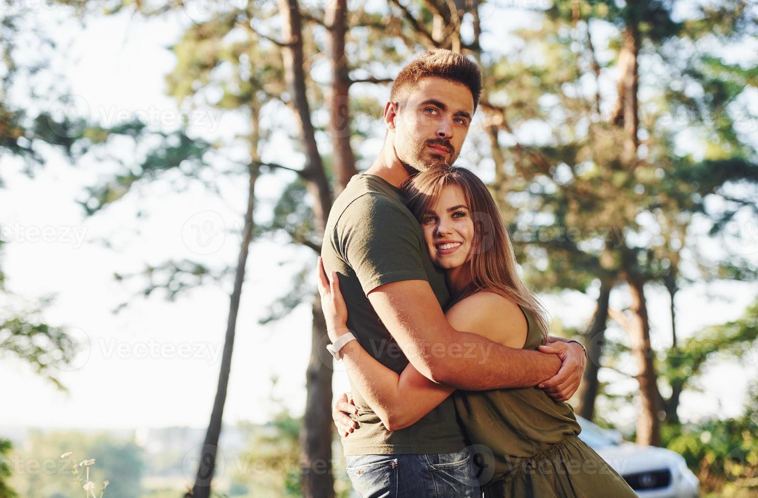 Happy together. Embracing each other. Beautiful young couple have a good time in the forest at daytime photo
