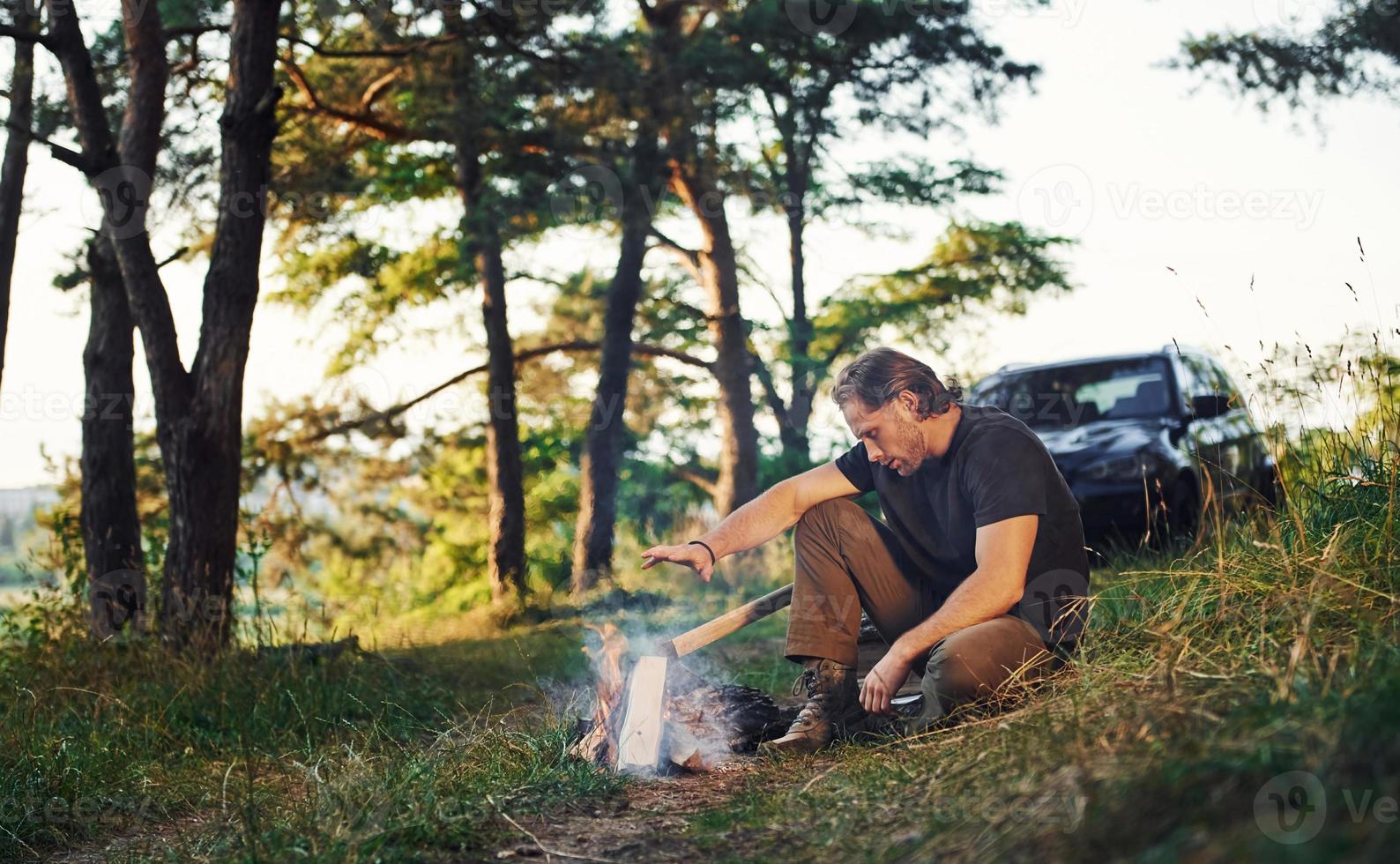 Heating by the fire. Man in black shirt near the campfire in the forest at his weekend time photo