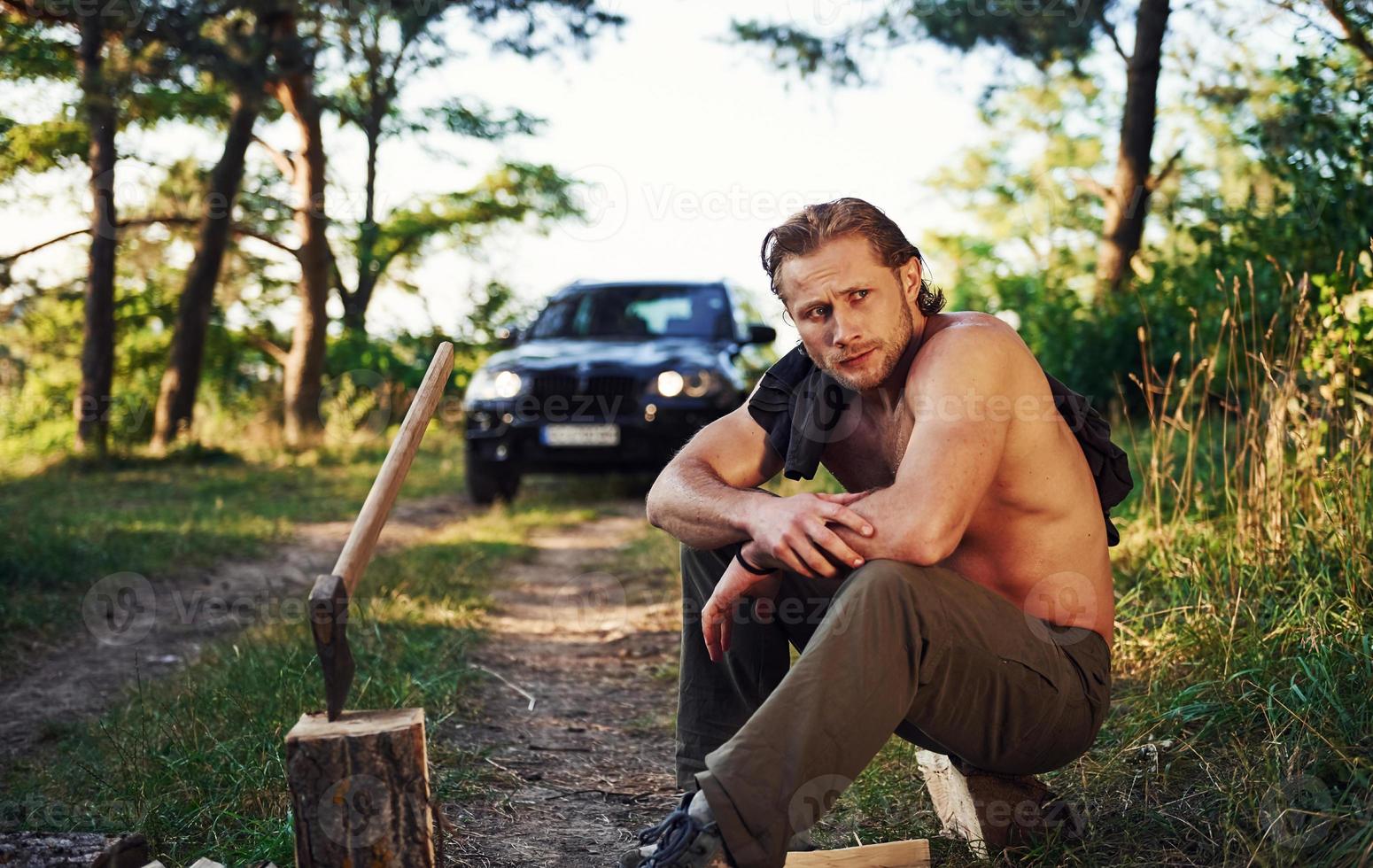 Woodsman have a rest. Handsome shirtless man with muscular body type is in the forest at daytime photo