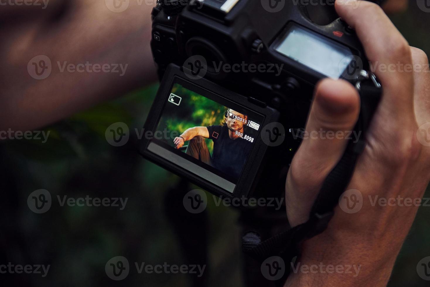 Photographer's hands holds camera. Backstage of photoshoot in the forest. Man in black shirt photo