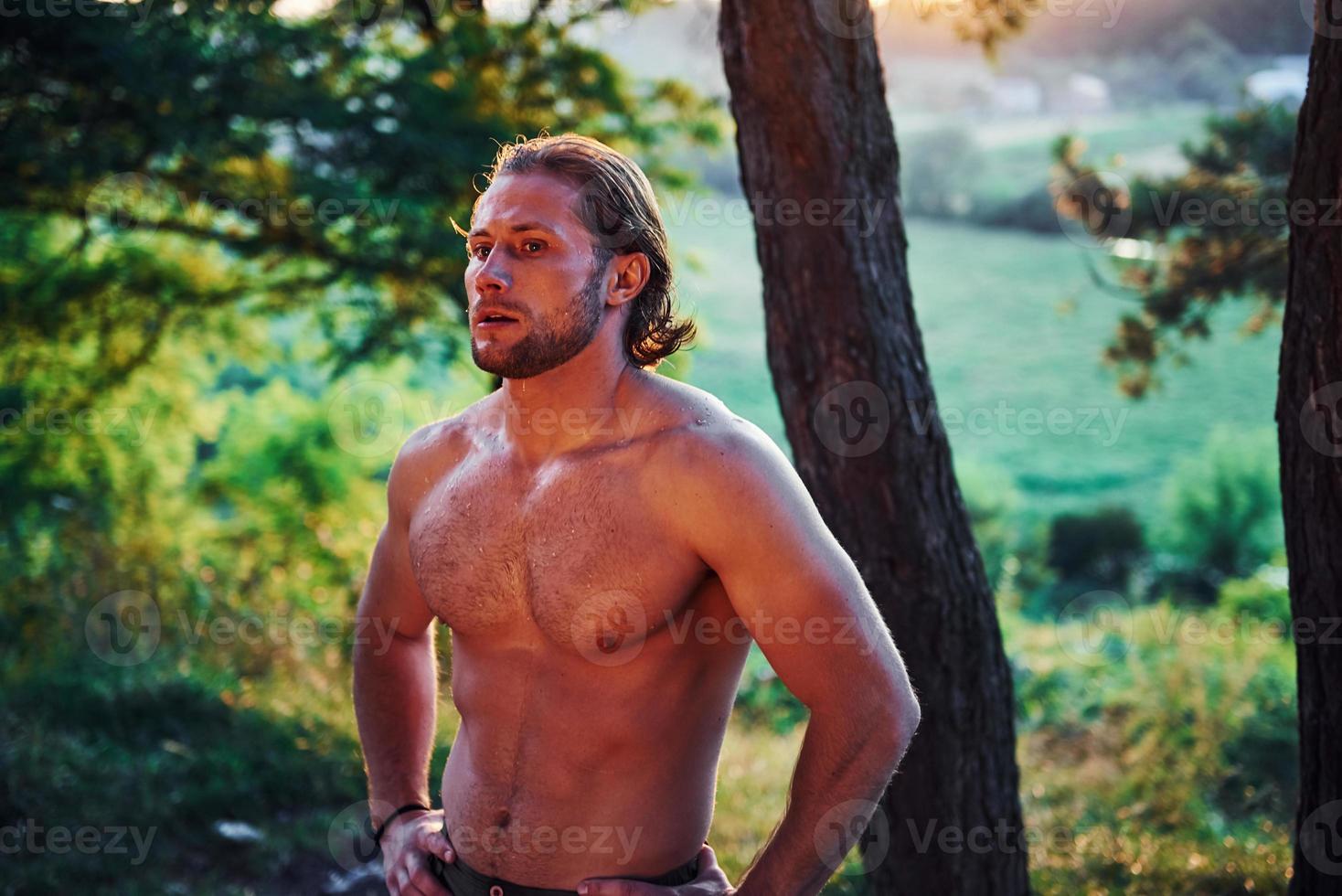 Beautiful nature. Handsome shirtless man with muscular body type is in the forest at daytime photo