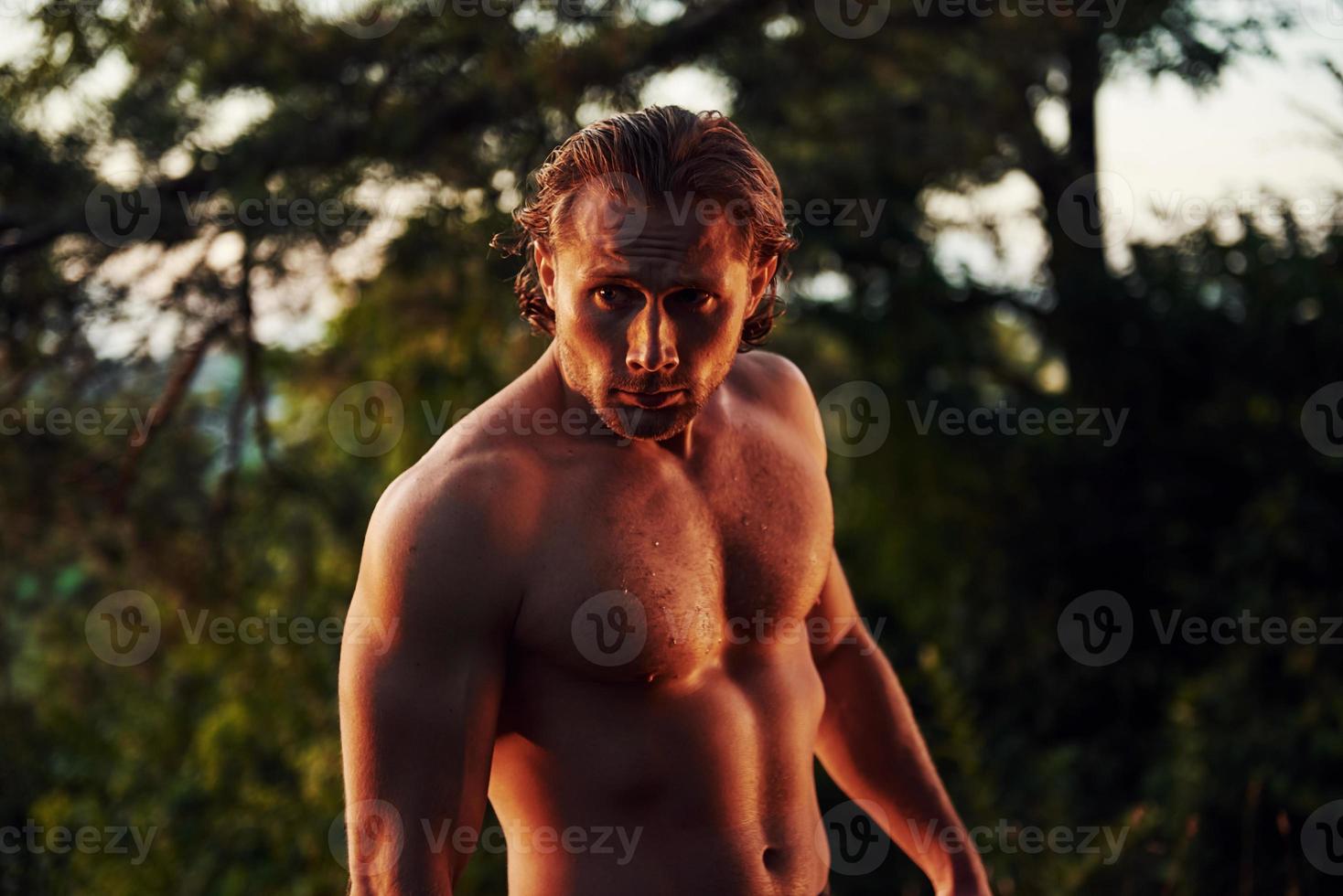 Handsome shirtless man with muscular body type is in the forest at daytime photo