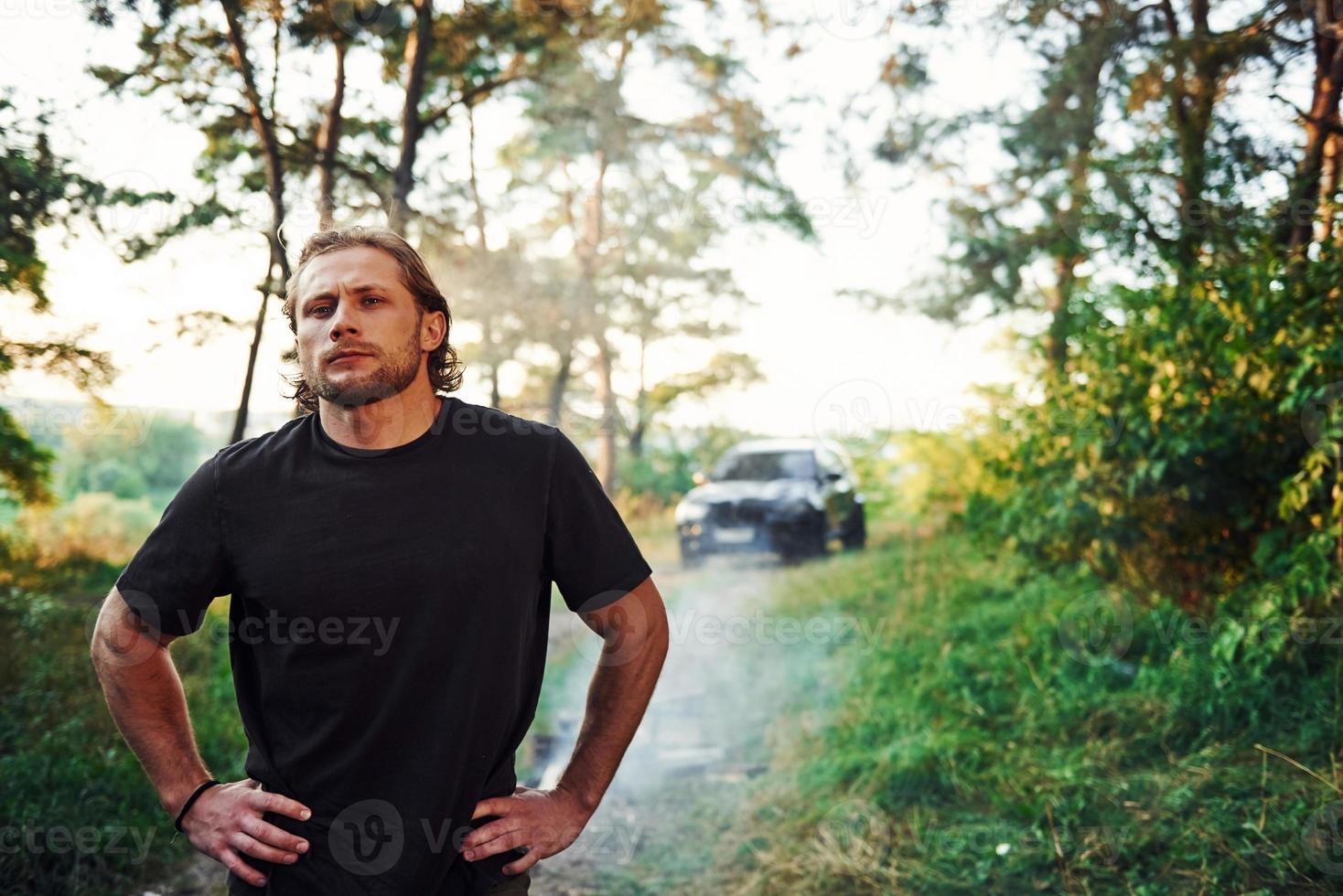 retrato de hombre que se para en el bosque y mira la naturaleza. automóvil estacionado detrás foto