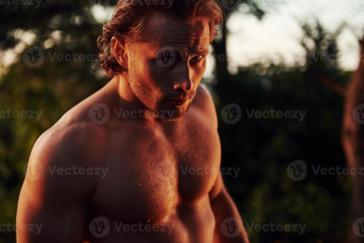 Handsome shirtless man with muscular body type is in the forest at daytime photo