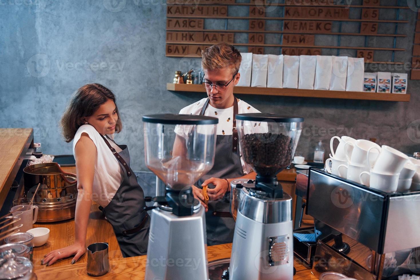 Behind the coffee machine. Two young workers indoors. Conception of business and service photo