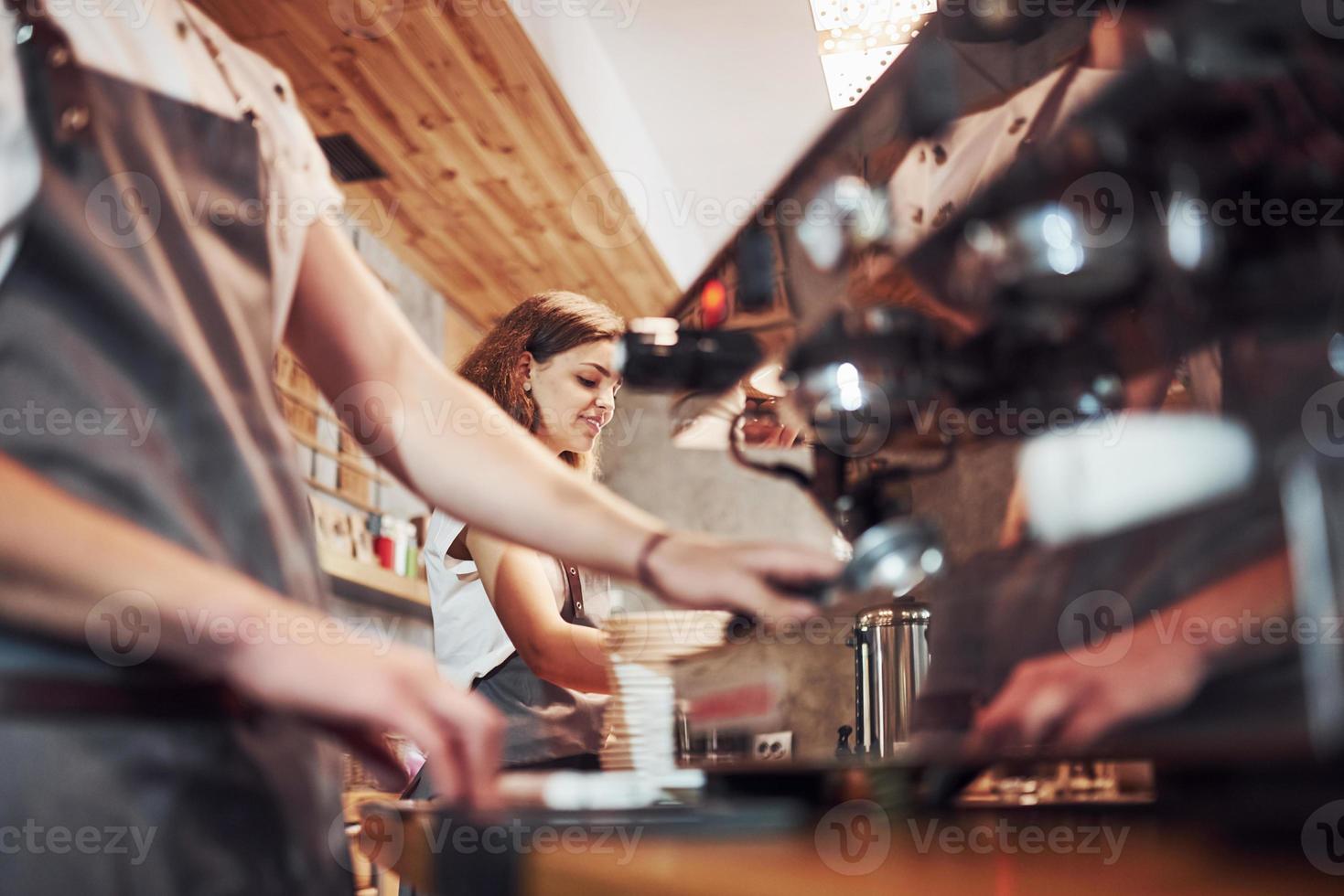 Process of making fresh drink. With machine. Two young cafe workers indoors. Conception of business and service photo