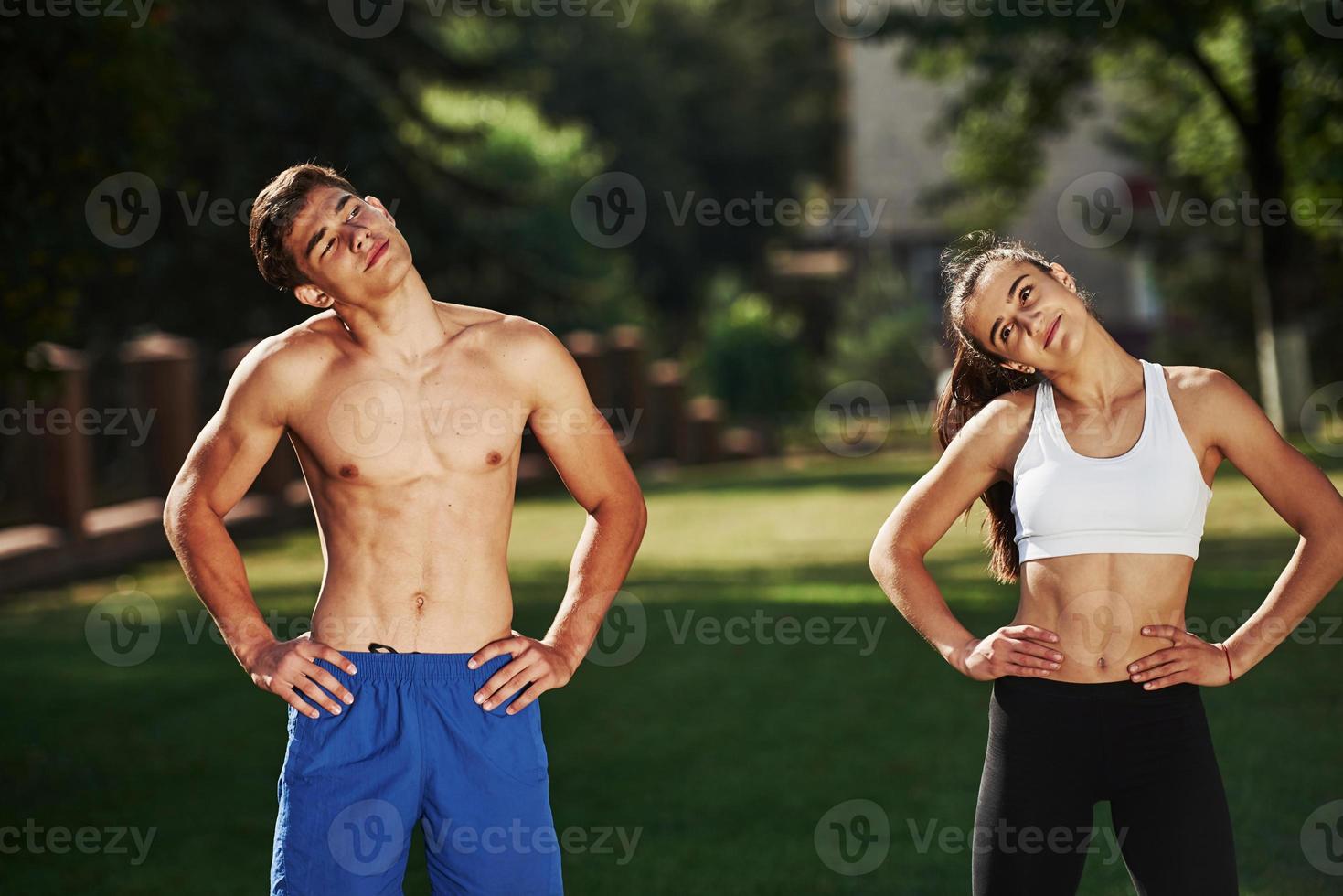 Warm up exercises. Man and woman have fitness day in the city at daytime in the park photo