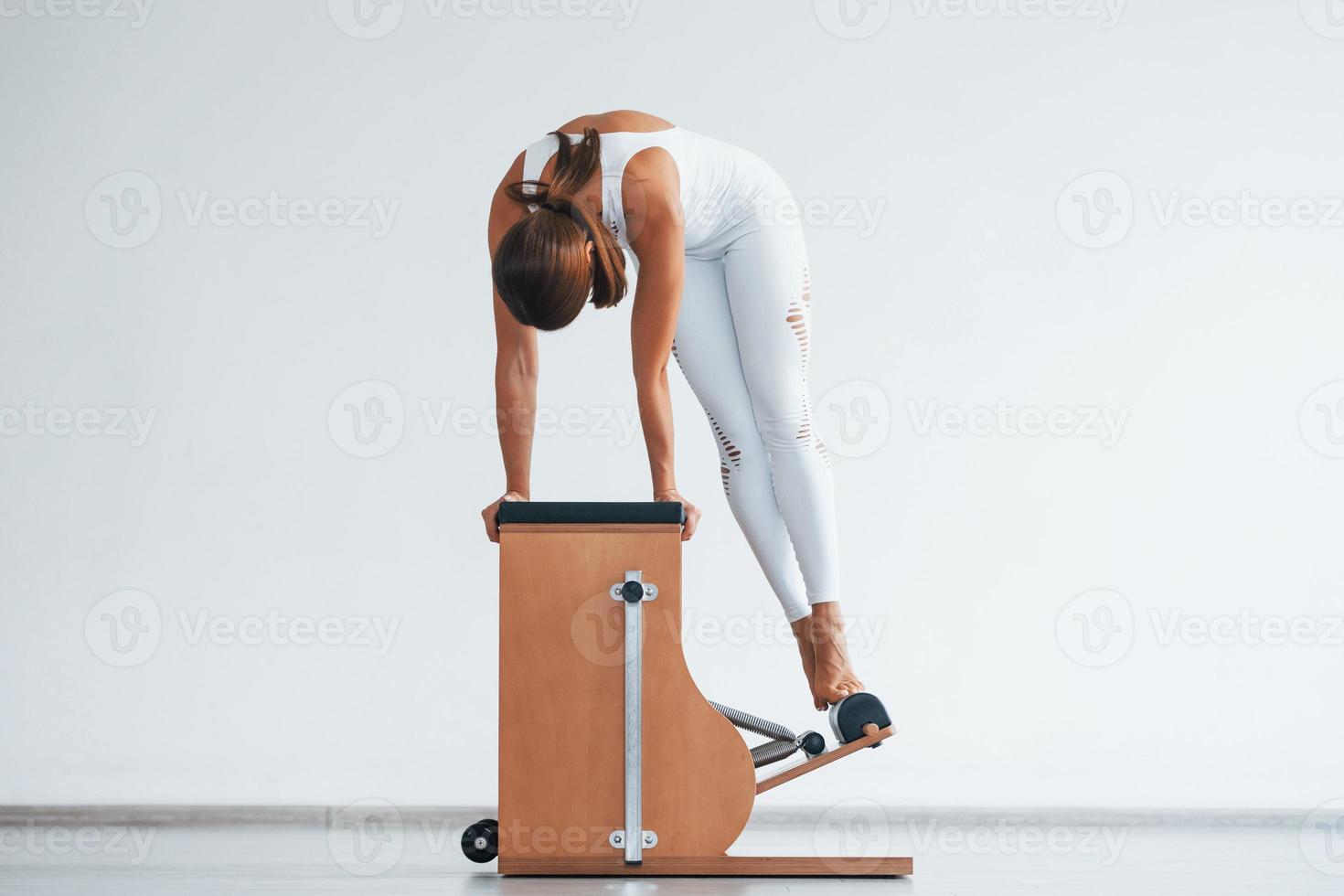 Confident young sporty woman with slim body type in the healthy center doing exercises by using special equipment photo