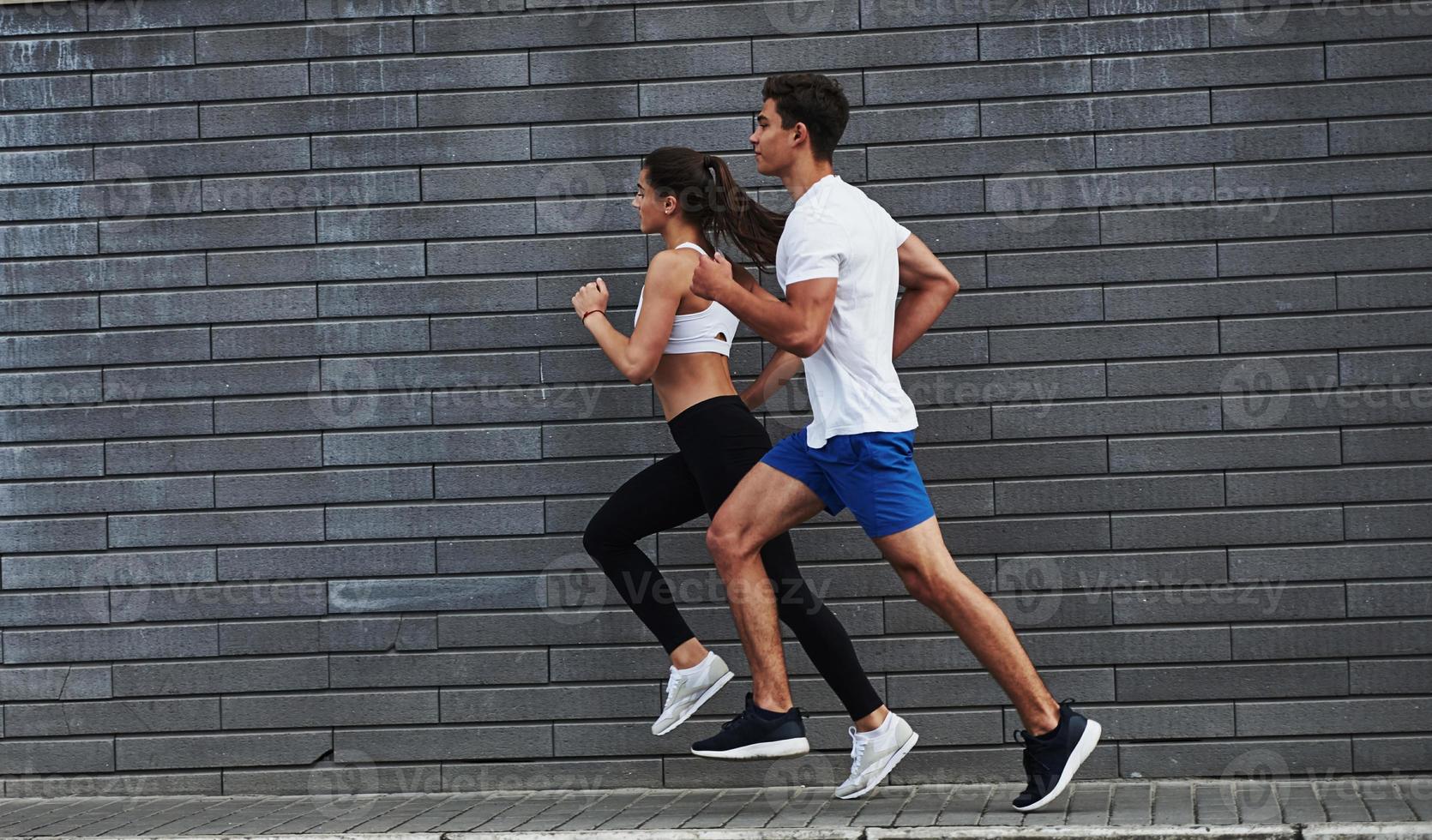 Healthy lifestyle. Man and woman have fitness day and running in the city at daytime near brick wall photo