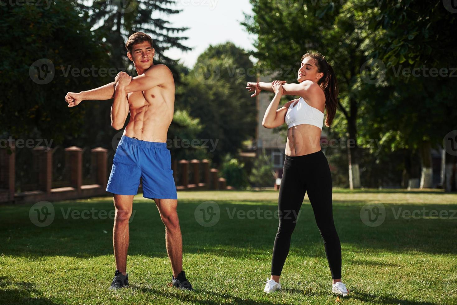 Warm up exercises. Man and woman have fitness day in the city at daytime in the park photo