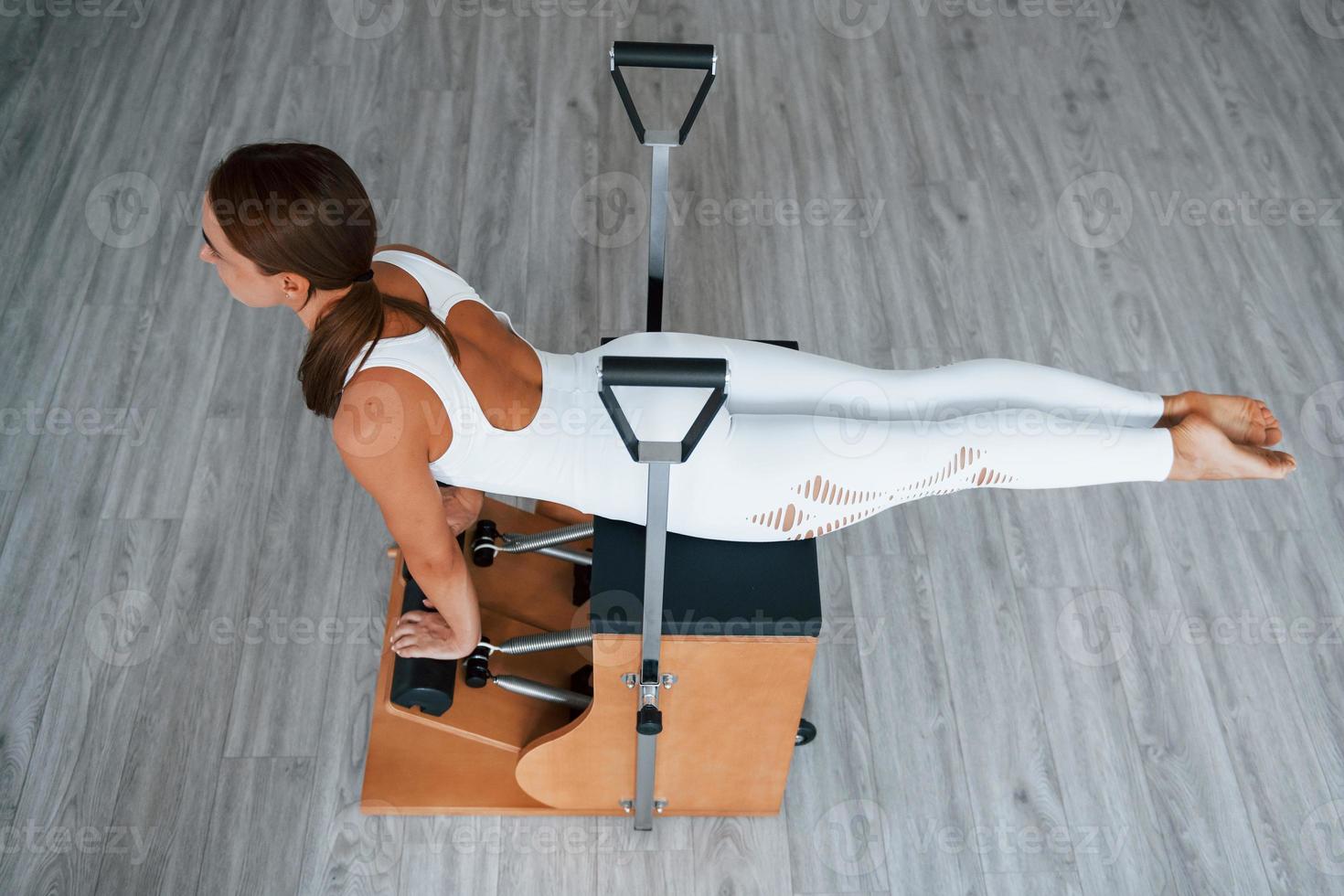 Aerial view. Confident young sporty woman with slim body type in the healthy center doing exercises by using special equipment photo
