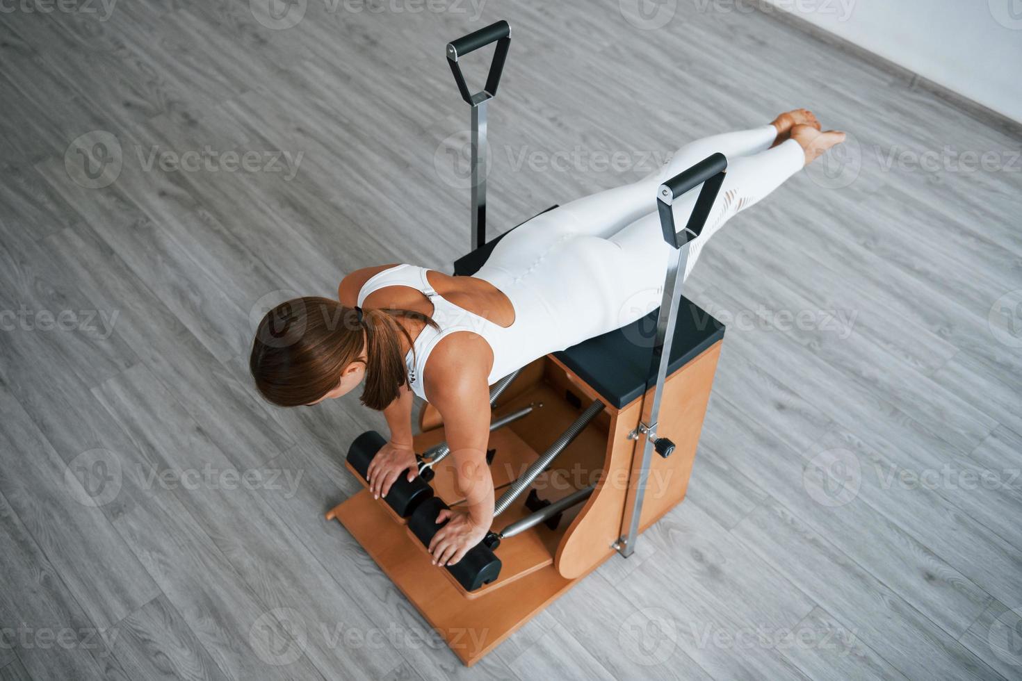 Aerial view. Confident young sporty woman with slim body type in the healthy center doing exercises by using special equipment photo