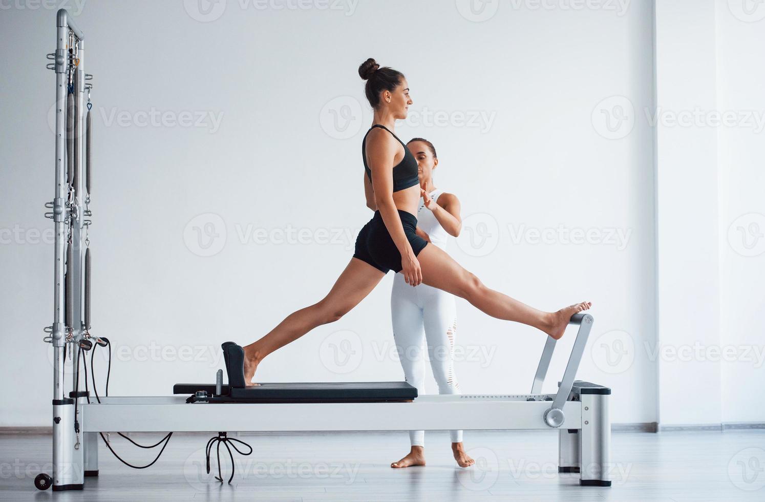 Trainer helps sporty woman with slim body type in the healthy center to do exercises by using special equipment photo