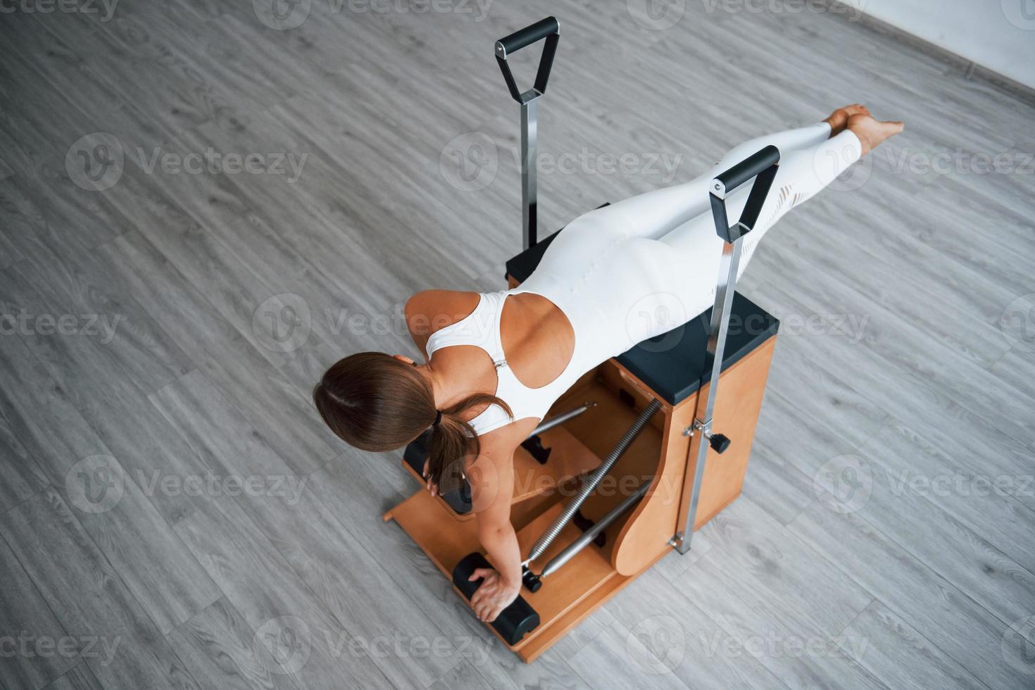 Aerial view. Confident young sporty woman with slim body type in the healthy center doing exercises by using special equipment photo
