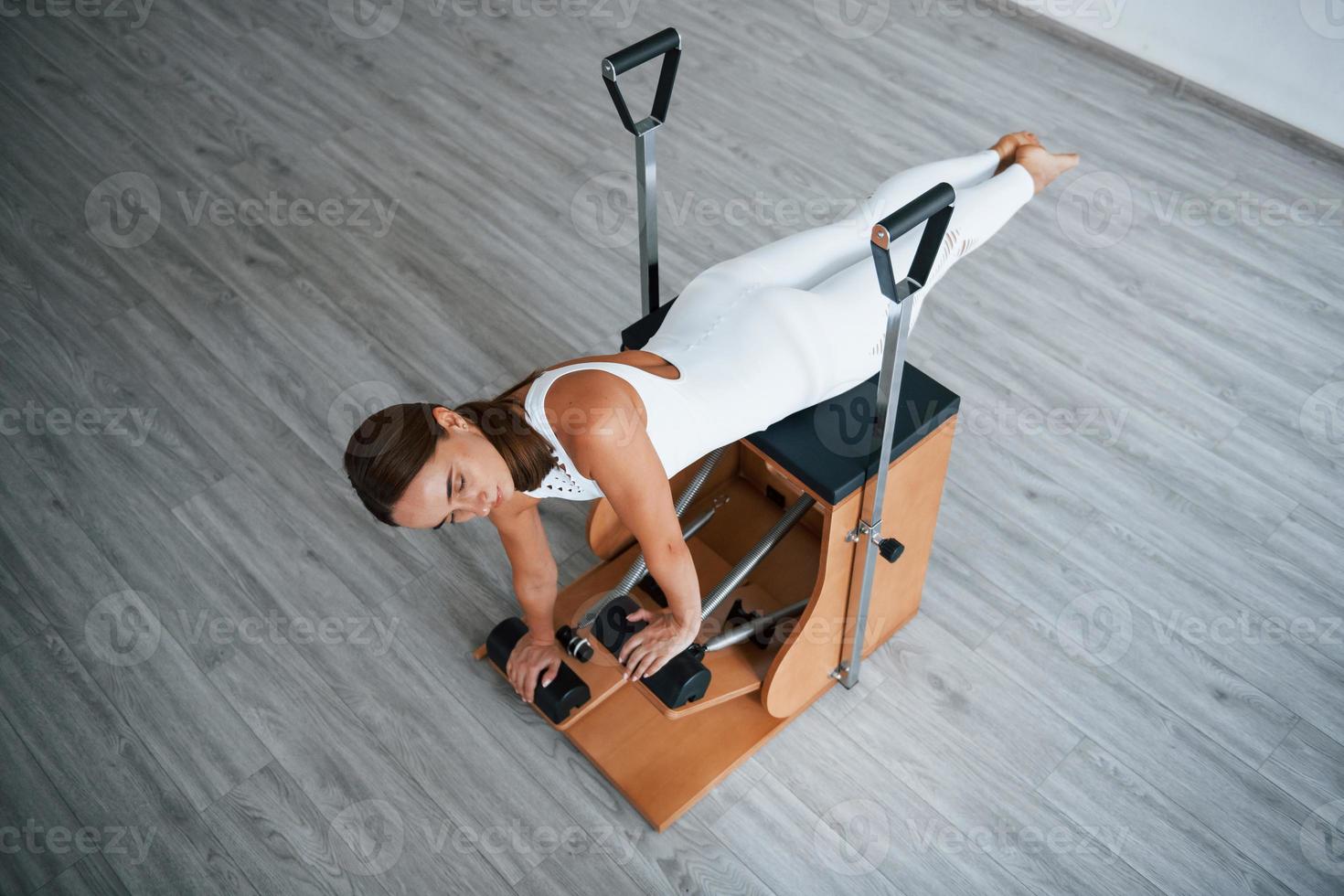 Aerial view. Confident young sporty woman with slim body type in the healthy center doing exercises by using special equipment photo
