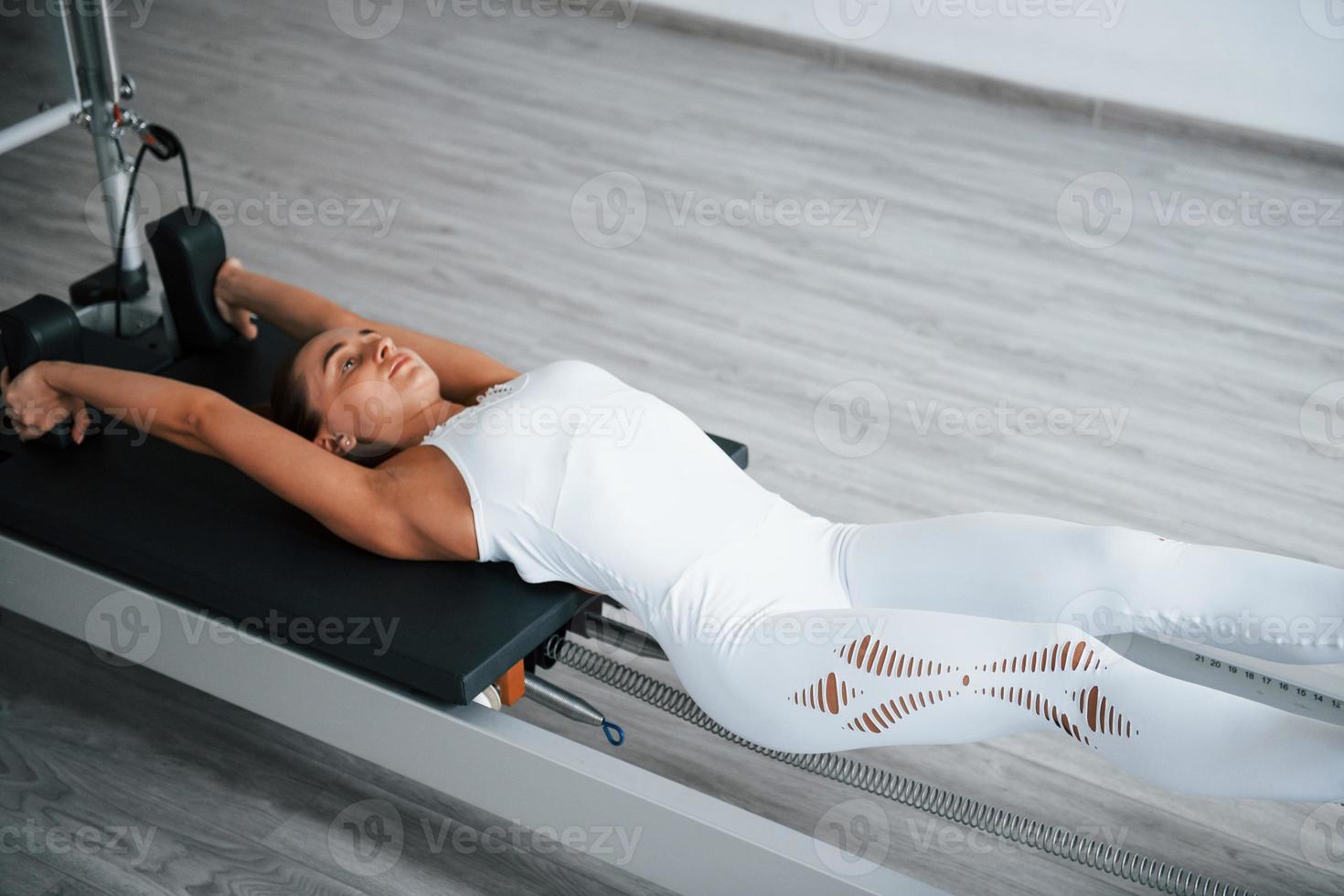 Working hard. Confident young sporty woman with slim body type in the healthy center doing exercises by using special equipment photo
