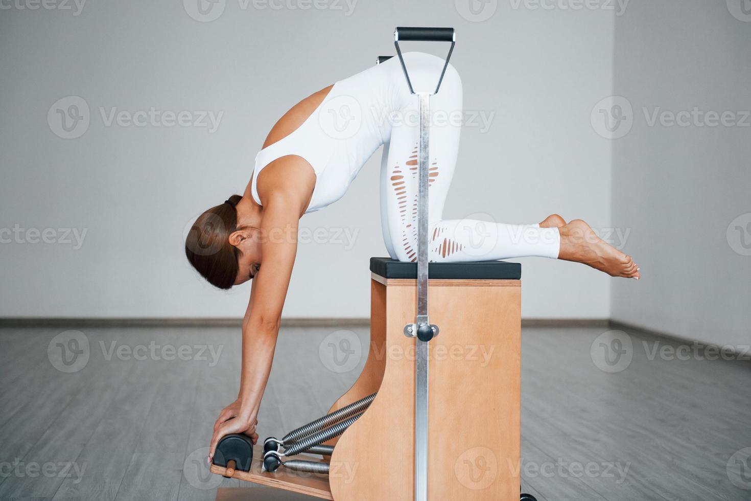 Side view. Confident young sporty woman with slim body type in the healthy center doing exercises by using special equipment photo