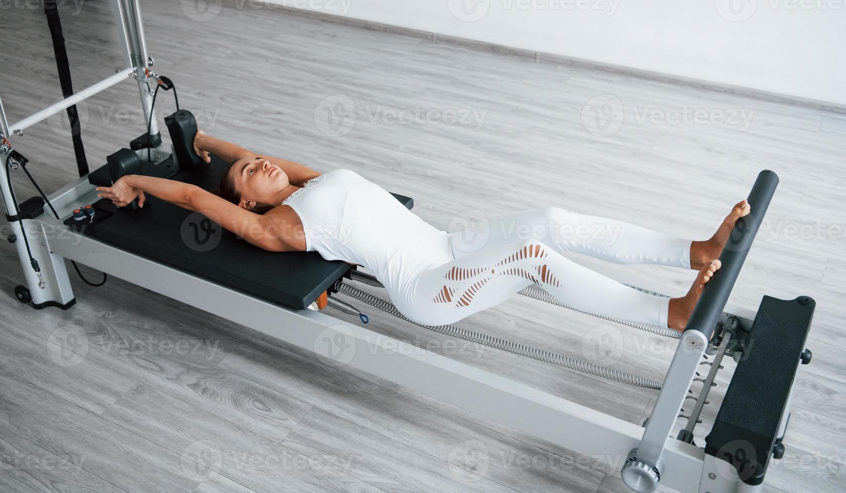 Working hard. Confident young sporty woman with slim body type in the healthy center doing exercises by using special equipment photo