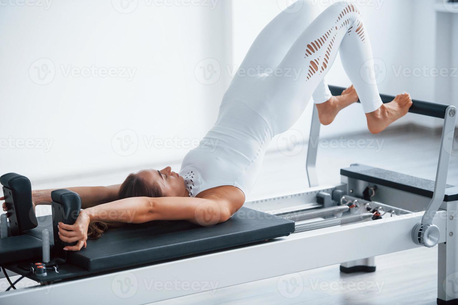 Good for the spine. Confident young sporty woman with slim body type in the healthy center doing exercises by using special equipment photo