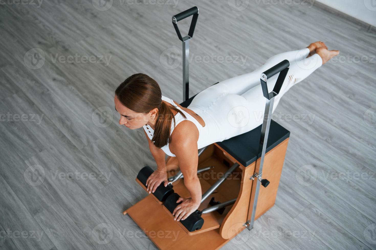Aerial view. Confident young sporty woman with slim body type in the healthy center doing exercises by using special equipment photo