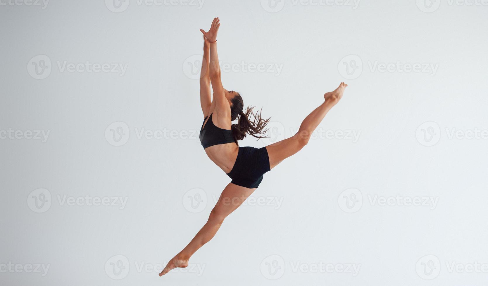 Photo in motion. Young sporty woman in black clothes with slim body type in the healthy center doing exercises