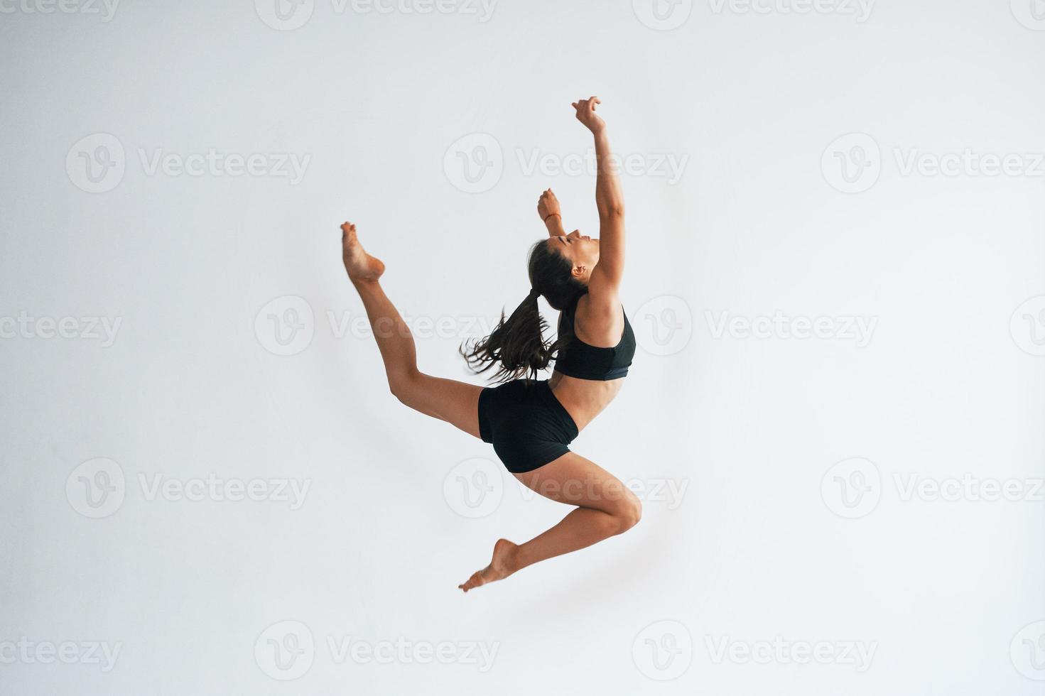Doing crazy tricks. Young sporty woman in black clothes with slim body type in the healthy center doing exercises photo