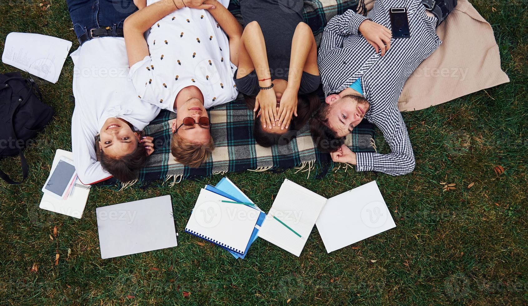 Having good rest. Group of young students in casual clothes on green grass at daytime photo