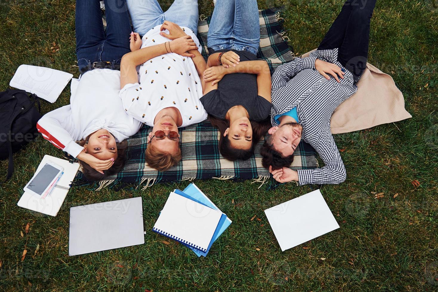 Having good rest. Group of young students in casual clothes on green grass at daytime photo