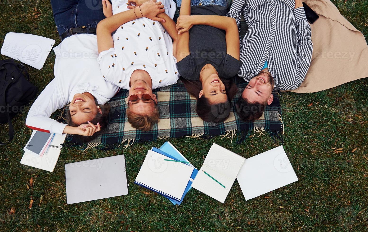 Having good rest. Group of young students in casual clothes on green grass at daytime photo