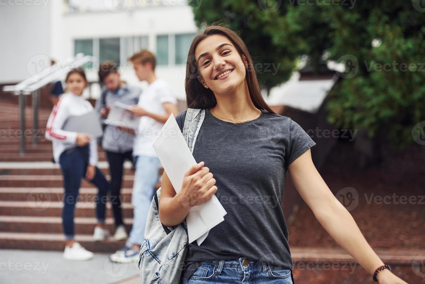 chica positiva frente a amigos. grupo de jóvenes estudiantes con ropa informal cerca de la universidad durante el día foto