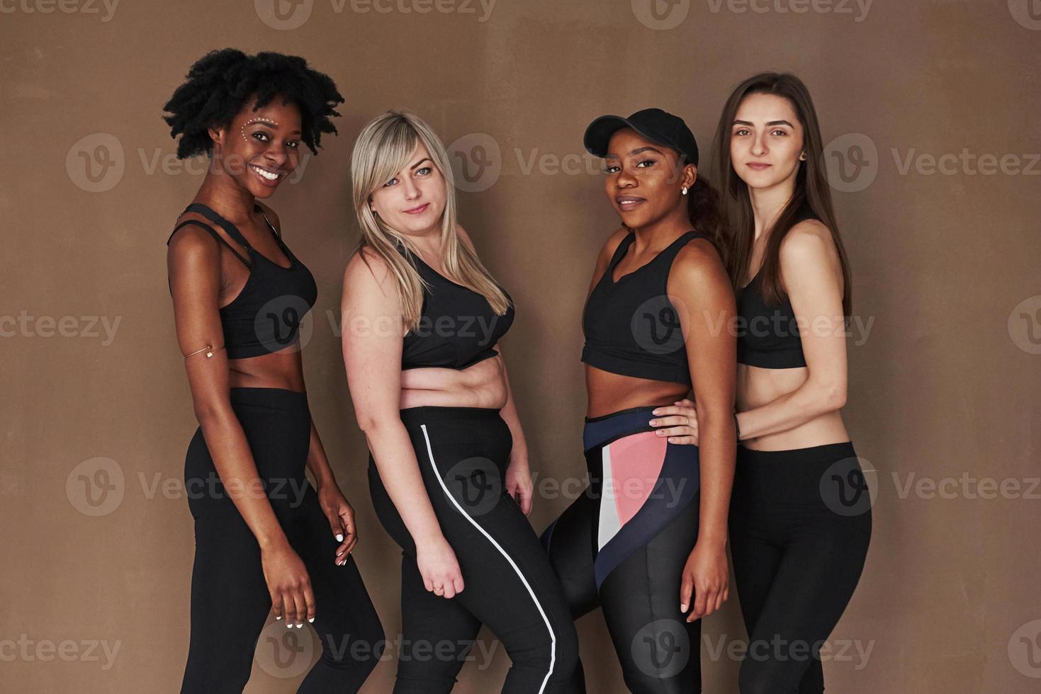 Everyone is beautiful on his own way. Group of multi ethnic women standing in the studio against brown background photo