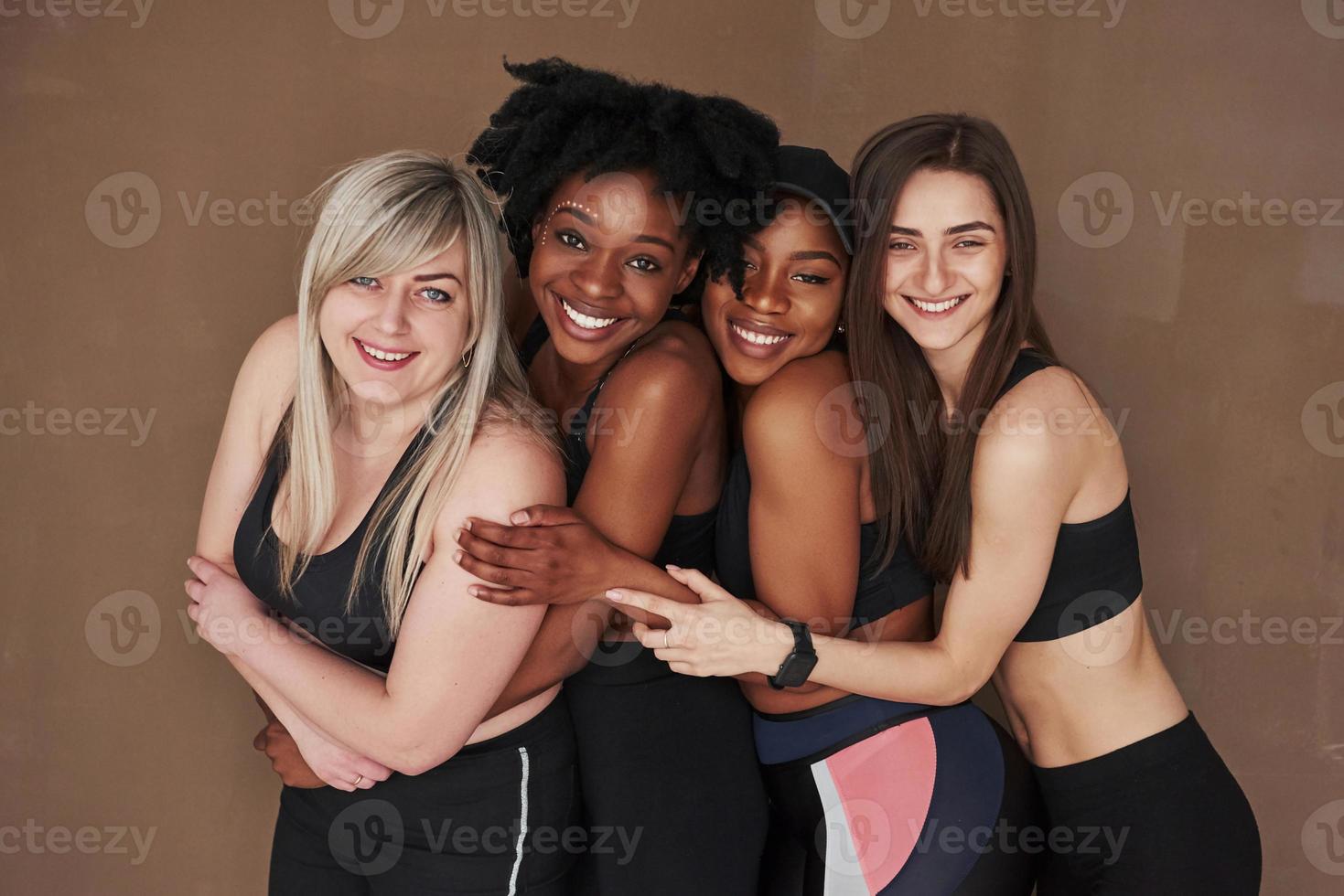 Leaning to the front of them. Group of multi ethnic women standing in the studio against brown background photo