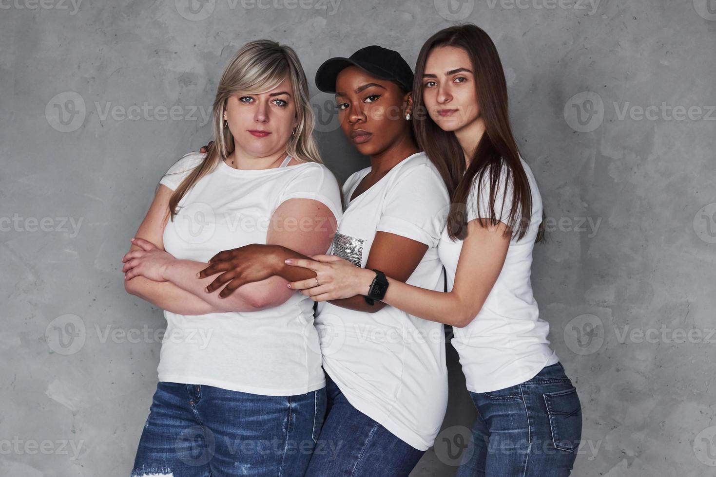 Three people together. Group of multi ethnic women standing in the studio against grey background photo