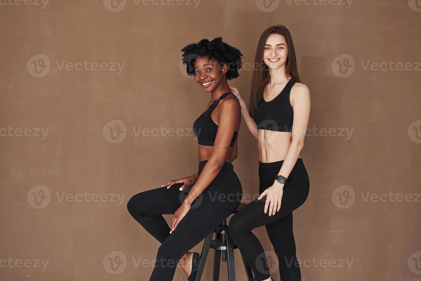 Facial expressions. Two multi ethnic female friends stands in the studio with brown background photo