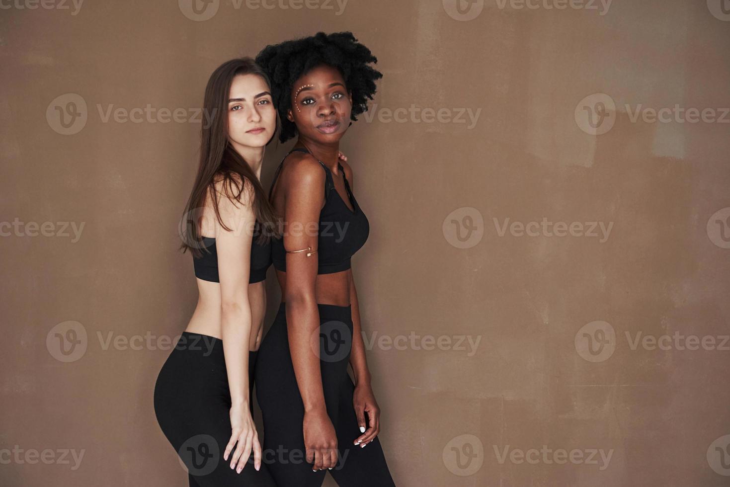 dos amigas multiétnicas se paran en el estudio con antecedentes marrones foto