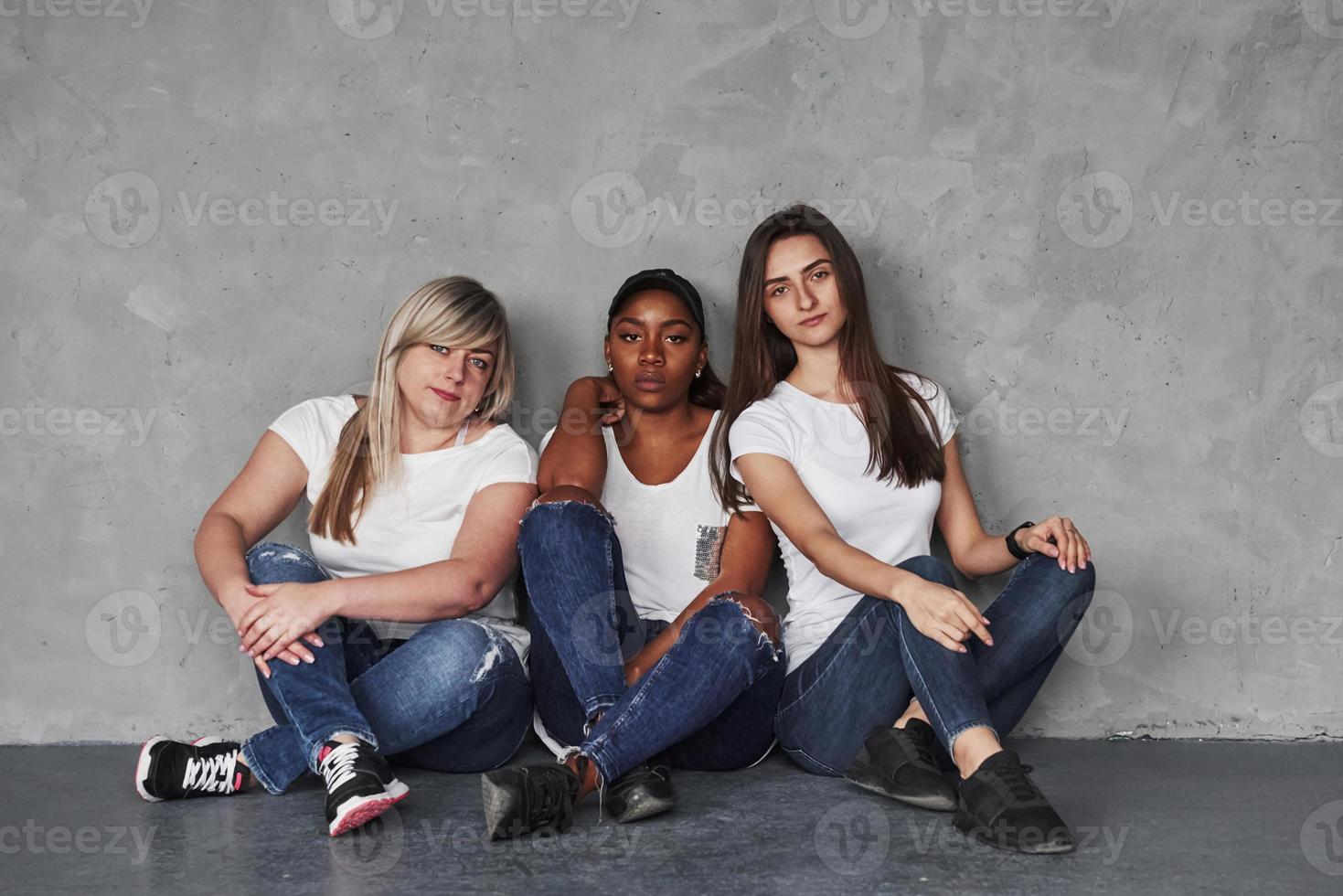 African american girl is serious. Group of multi ethnic women sitting in the studio against grey background photo
