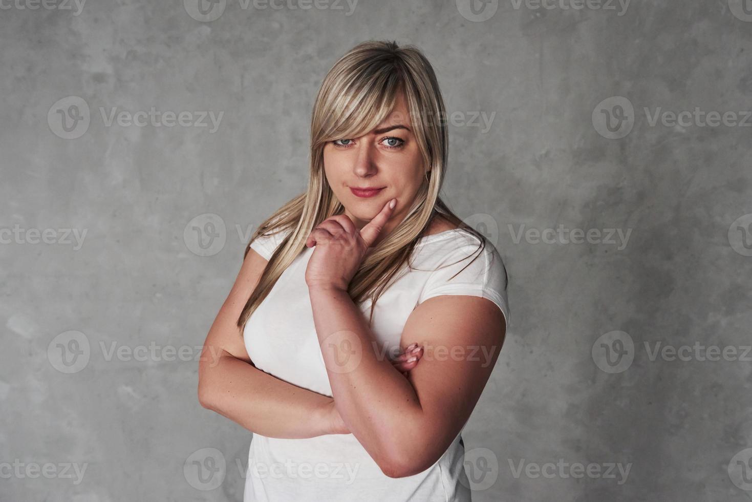 Thoughtful look. Young white woman in the studio standing against grey background photo