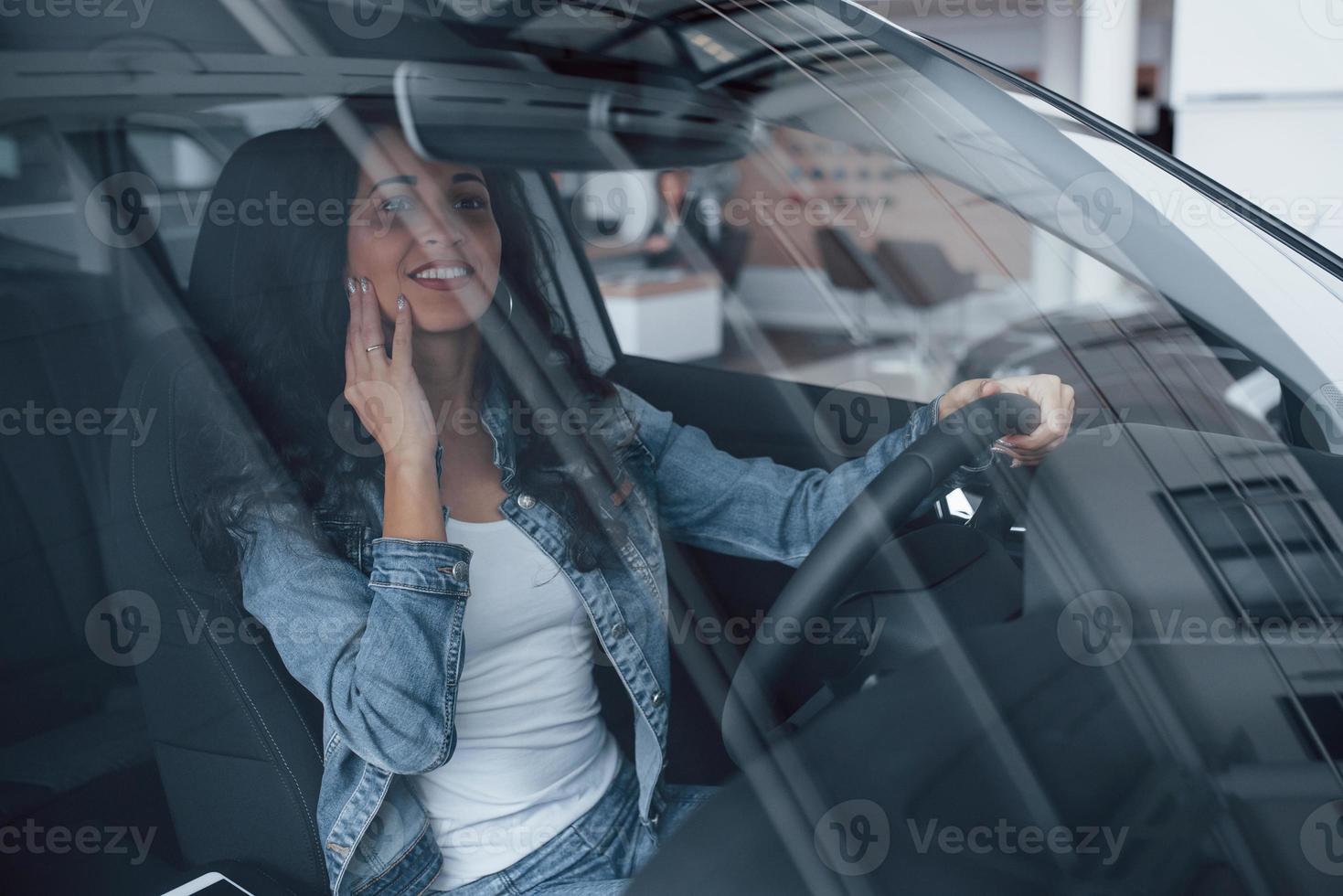 Not bad at all. Cute girl with black hair trying her brand new expensive car in the automobile salon photo