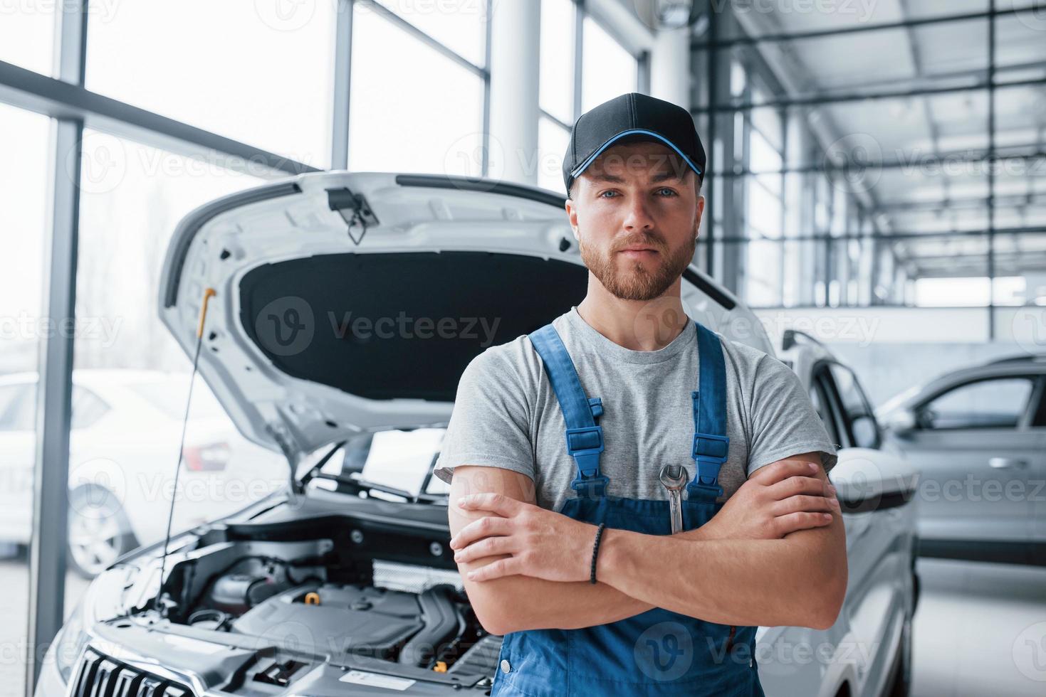 Serious look. Employee in the blue colored uniform stands in the automobile salon photo