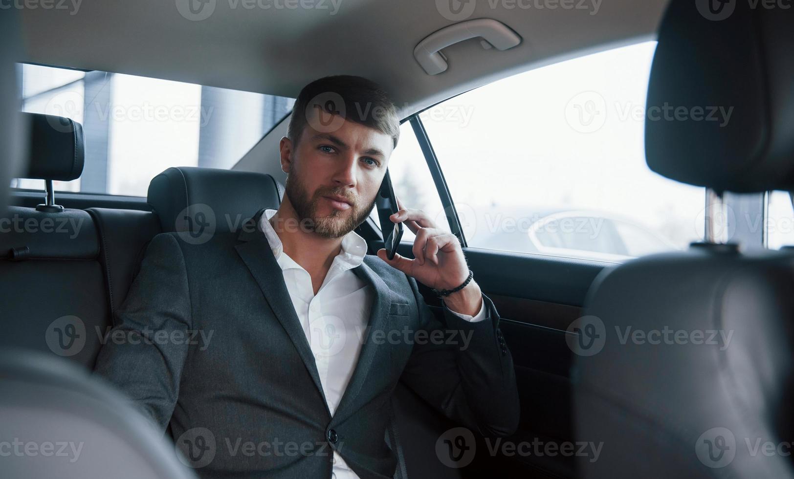 Waiting for the answer. Businessman in official wear have call when sitting on the back of car photo