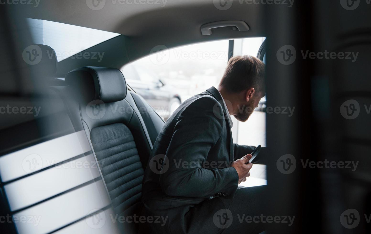 Getting out of the vehicle. Businessman in official wear have call when sitting on the back of car photo