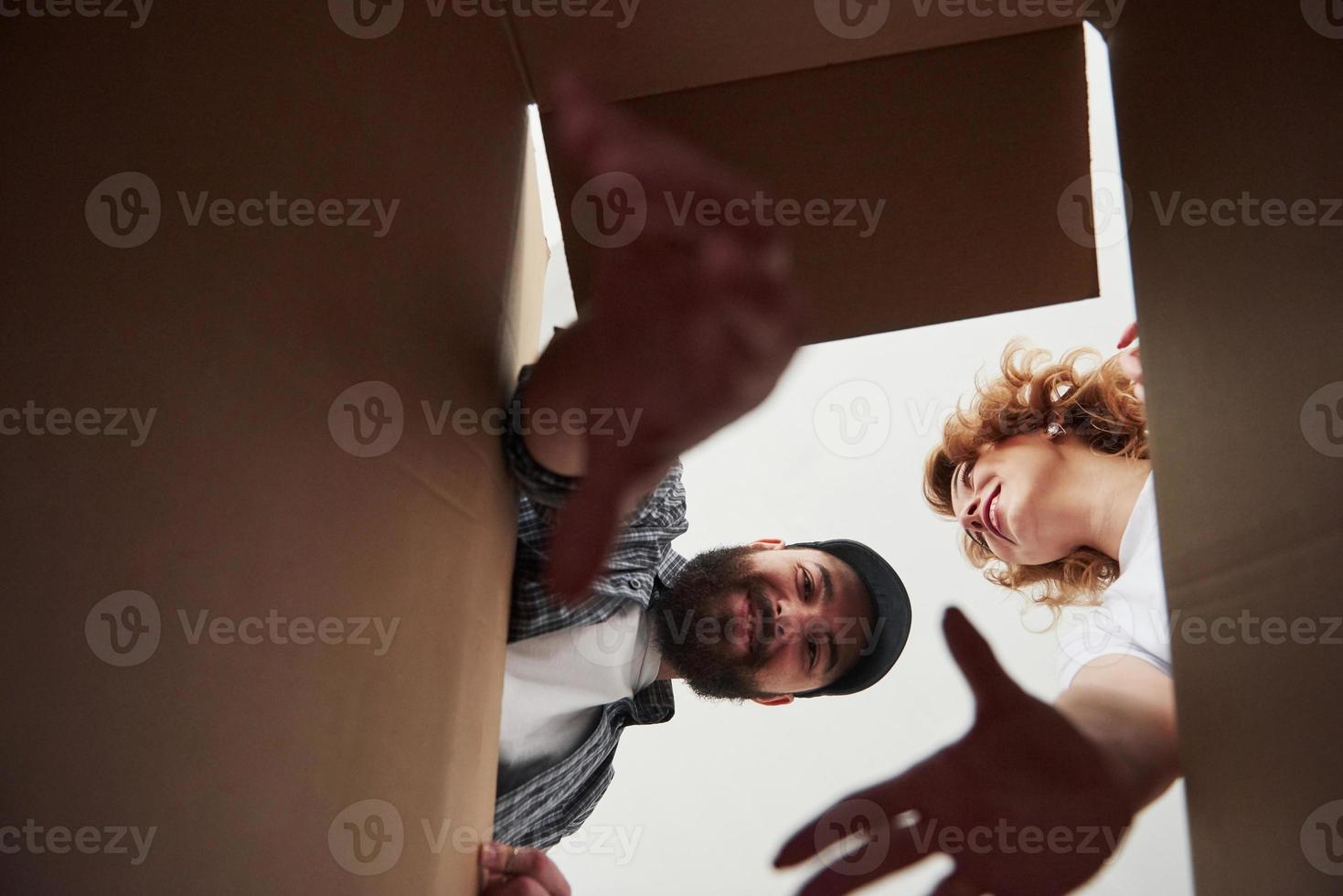 hombre barbudo tratando de alcanzar el artículo de una caja. pareja feliz juntos en su nueva casa. concepción de movimiento foto