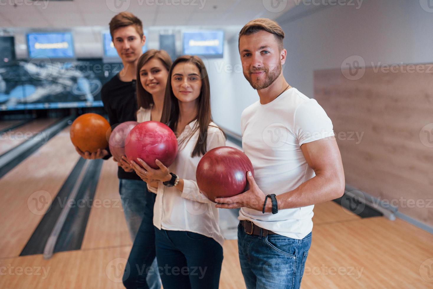 Looking into the camera. Young cheerful friends have fun in bowling club at their weekends photo