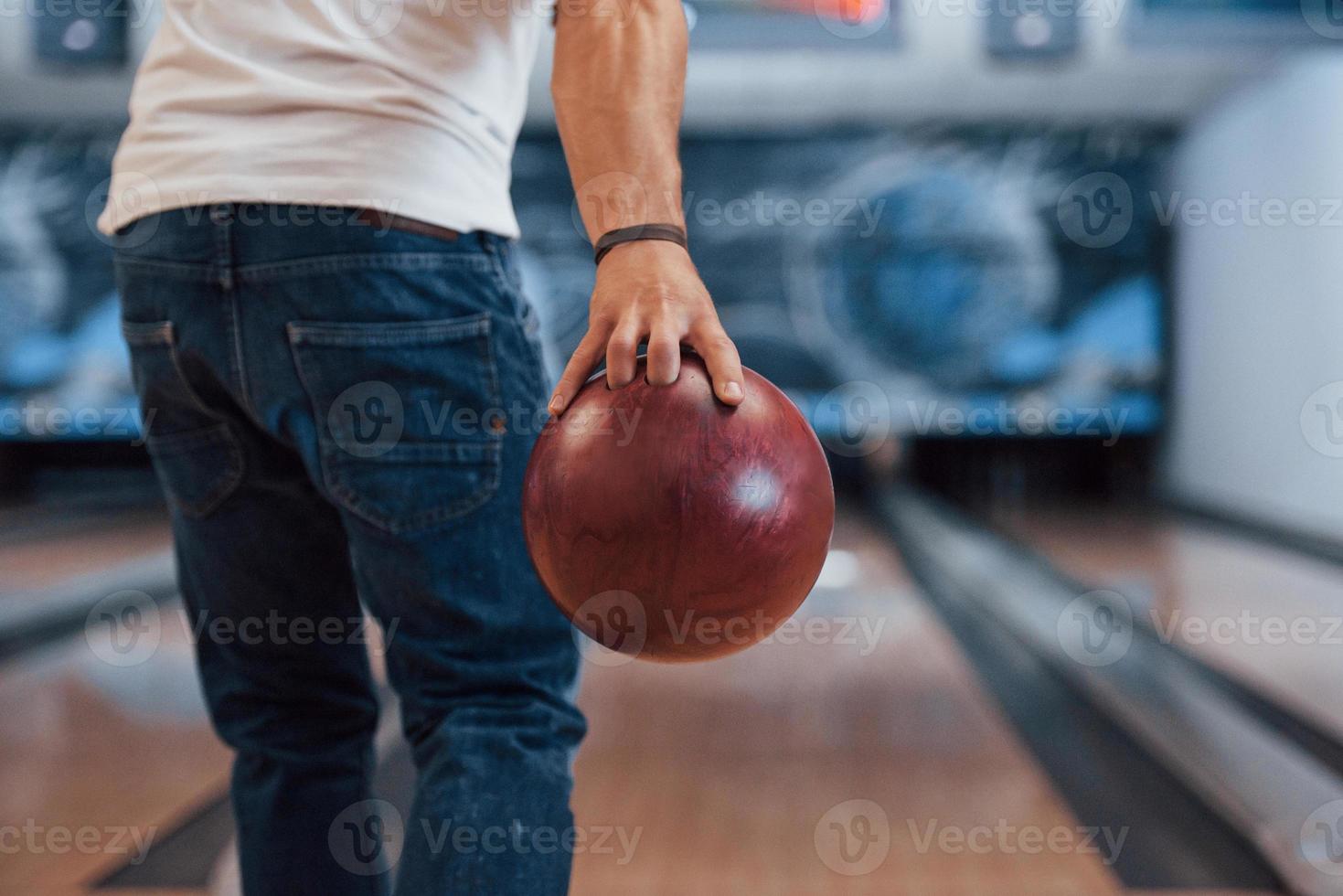This is gonna be the strike. Rear particle view of man in casual clothes playing bowling in the club photo