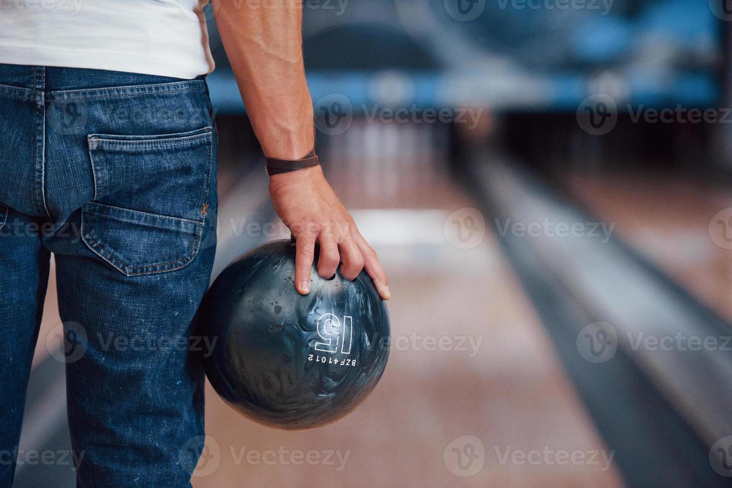 Focused photo. Rear particle view of man in casual clothes playing bowling in the club photo